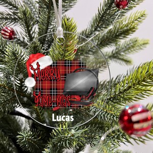 May include: A round, clear Christmas ornament with a red and black plaid background. The ornament features a Santa hat with reindeer antlers, the text "Merry Game-Mas", and a computer monitor with headphones. The name "Lucas" is printed at the bottom of the ornament.