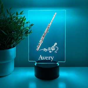 Peut inclure: Une veilleuse LED bleue avec une image blanche d'une flûte et de notes de musique. Le nom "Avery" est imprimé sous l'image.
