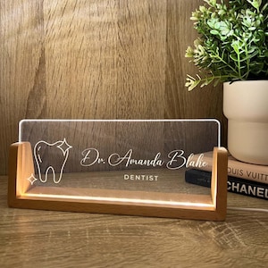 May include: A light-up acrylic sign with a wooden base. The sign features a tooth graphic and the name "Dr. Amanda Blake, Dentist" in white script. The wooden base emits a warm light.