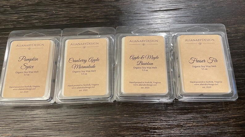 May include: Four clear plastic containers with labels for different scented soy wax melts. The scents are Pumpkin Spice, Cranberry Apple Marmalade, Apple & Maple Bourbon, and Fraser Fir. Each container is labeled with the name of the scent, "Organic Soy Wax Melt", and the size, 1.5 oz. The labels also include the company name, "ALIANABYDESIGN", and the website address, www.alianabydesign.net.