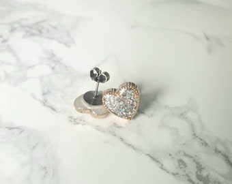 May include: A pair of silver heart-shaped earrings with clear sparkly stones. The earrings have a post back.