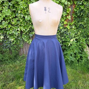 May include: A navy blue midi skirt with a full circle shape. The skirt is made of a smooth, cotton fabric and has a high waist.