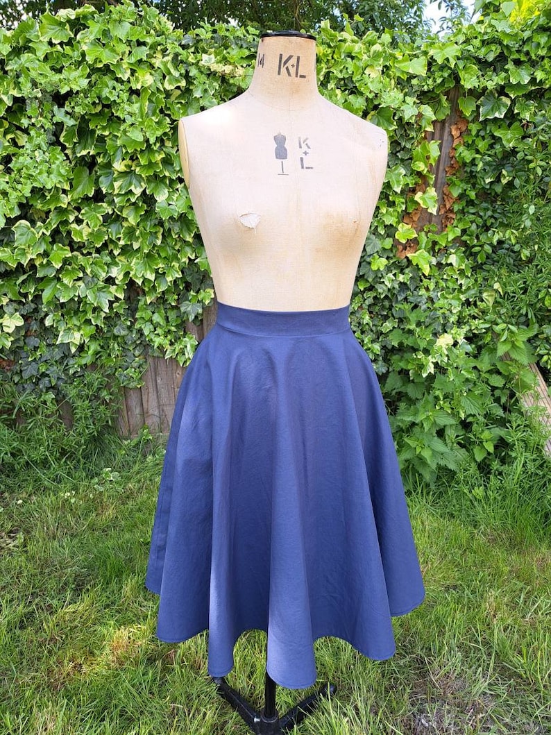 May include: A navy blue midi skirt with a full circle shape. The skirt is made of a smooth, cotton fabric and has a high waist.