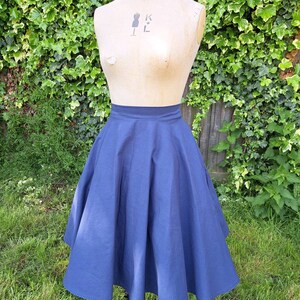 May include: A navy blue full circle skirt with a fitted waist. The skirt is made of a smooth, lightweight fabric and falls to just below the knee.