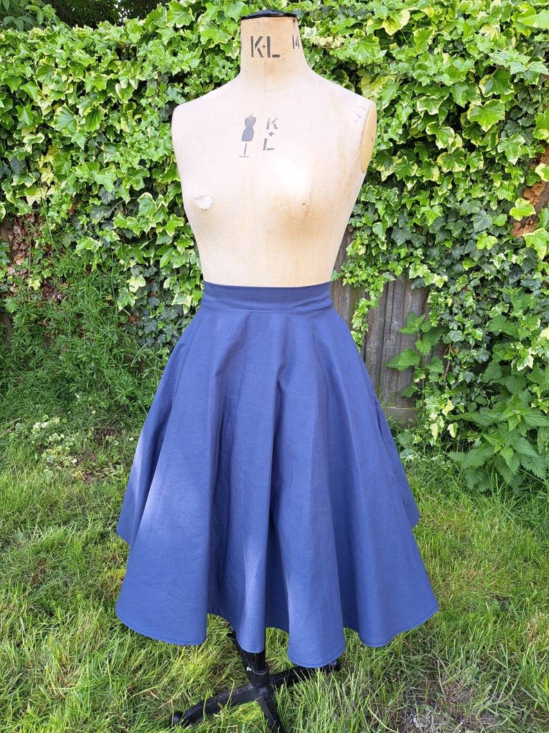 May include: A navy blue full circle skirt with a fitted waist. The skirt is made of a smooth, lightweight fabric and falls to just below the knee.