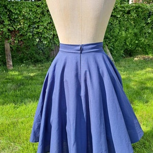 May include: A full-length view of a blue midi skirt with a high waist and a full circle shape. The skirt is made of a smooth, lightweight fabric and has a zipper closure in the back.