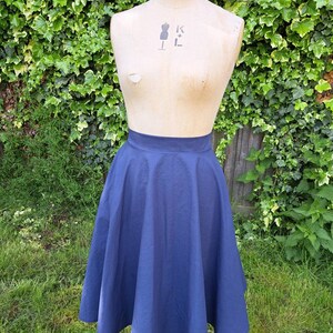 May include: A navy blue midi skirt with a full circle shape. The skirt is made of a smooth, cotton fabric and has a high waist.