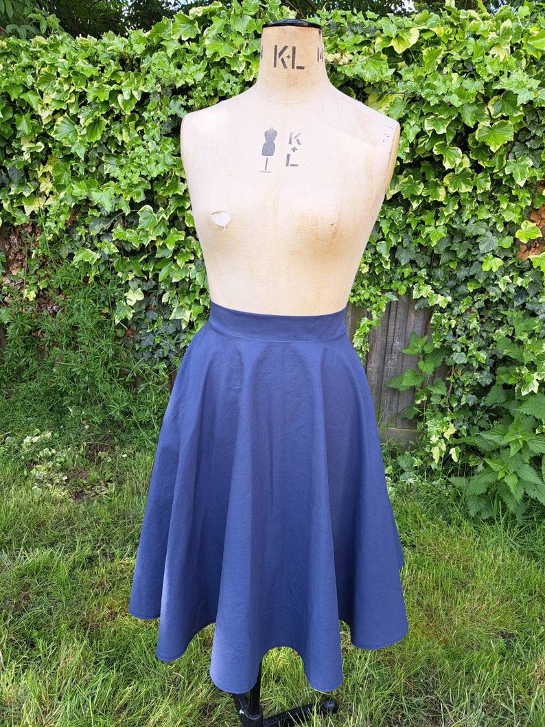 May include: A navy blue midi skirt with a full circle shape. The skirt is made of a smooth, cotton fabric and has a high waist.