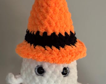 May include: A handmade crochet ghost doll with a bright orange witch hat trimmed with black. The ghost has large, sparkly eyes and small arms. The plush toy is white and is held in a hand.