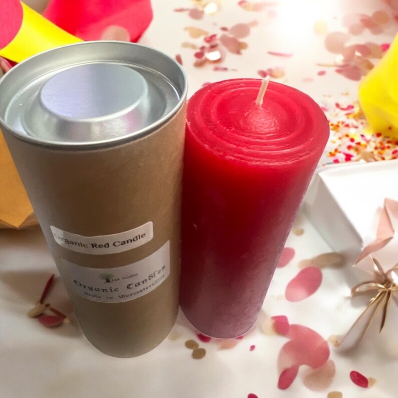 May include: A red candle in a cardboard tube with a silver lid. The tube has a label that says "Organic Red Candle" and "Organic Candles".
