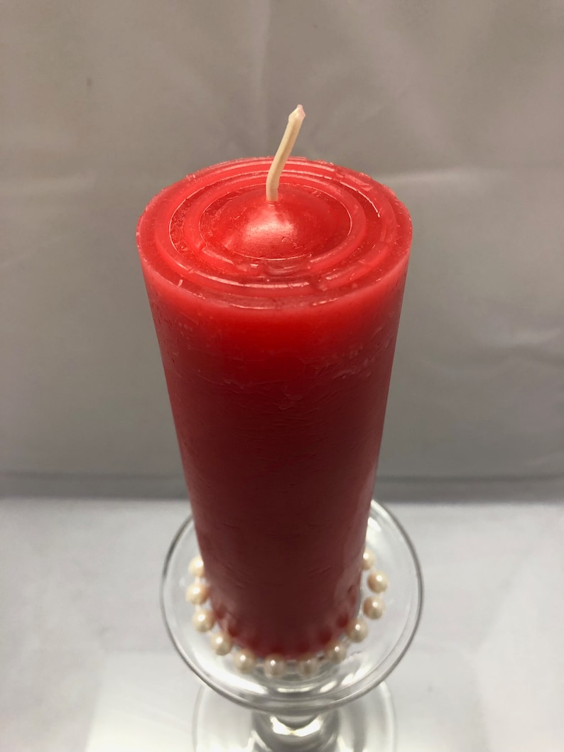 May include: A red pillar candle with a white wick sits on a glass candle holder with a white pearl trim.