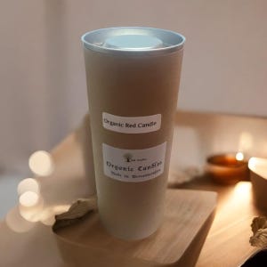 May include: A tall, cylindrical, light gray candle with a silver lid. The candle has a white label that says "Organic Red Candle" and a smaller white label that says "Organic Candles Made in Worcestershire".