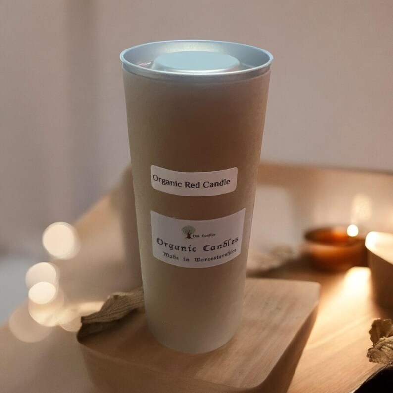 May include: A tall, cylindrical, light gray candle with a silver lid. The candle has a white label that says "Organic Red Candle" and a smaller white label that says "Organic Candles Made in Worcestershire".
