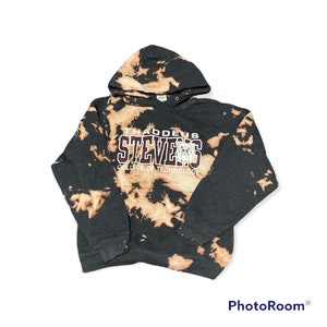 Puede incluir: Una sudadera con capucha de color negro y marrón tie-dye con el texto "Thaddeus Stevens College of Technology" en letras granate. La sudadera tiene una capucha con cordón y un bolsillo canguro.