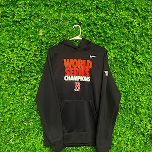 Peut inclure: Sweat-shirt à capuche noir avec l'inscription "World Series Champions" en lettres rouges et blanches. Un logo Nike blanc en forme de virgule est situé sur le côté droit de la poitrine. Un "B" rouge est centré sous le texte.