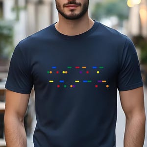 May include: A navy blue t-shirt with a rainbow colored braille message on the front. The message is "I love you" in braille.