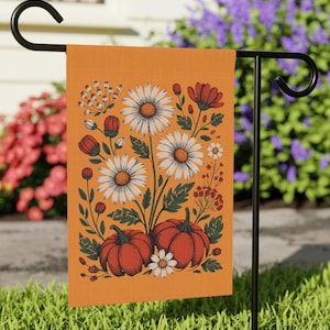 May include: Orange garden flag featuring a floral design with white daisies, red flowers, and orange pumpkins. The flag is displayed on a black metal stand, perfect for outdoor decor. The flag has the text "Fuck Trump".