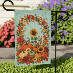 May include: A rectangular garden flag featuring a light blue background with a central arch of autumn foliage, sunflowers, and various pumpkins in shades of orange, cream, and green. The design includes red maple leaves and small berries.