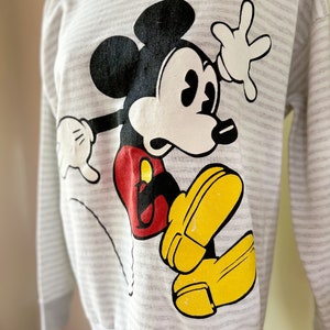 May include: A gray and white striped sweatshirt with a cartoon image of Mickey Mouse in black, white, red, and yellow.