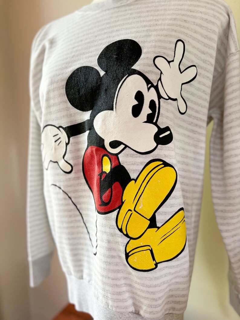 May include: A gray and white striped sweatshirt with a cartoon image of Mickey Mouse in black, white, red, and yellow.