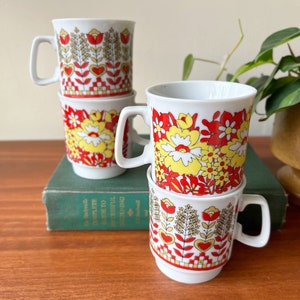 May include: Set of four white ceramic mugs with a floral pattern in red, yellow, and gold. The mugs are stacked on top of each other.