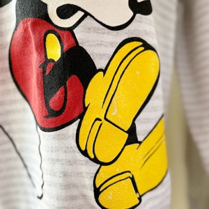 May include: A gray sweatshirt with a black and white cartoon image of Mickey Mouse. Mickey is wearing red shorts and yellow shoes. The sweatshirt has a striped pattern.
