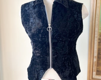 May include: A black velvet vest with a zipper closure and a pointed hem. The vest has a quilted pattern and a collar.