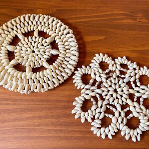 May include: Two white shell coasters, one round and one with a flower design, on a wooden surface.