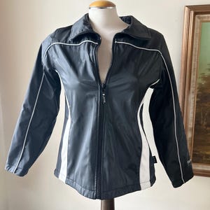 May include: Black and white windbreaker jacket with a zipper closure and white piping. The jacket has a stand-up collar and long sleeves.