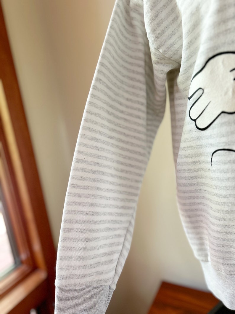 May include: A gray and white striped long-sleeve sweatshirt with a black and white cartoon hand design on the front.