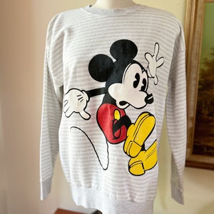 May include: A gray and white striped long-sleeved sweatshirt with a cartoon image of Mickey Mouse in red, black, and yellow.