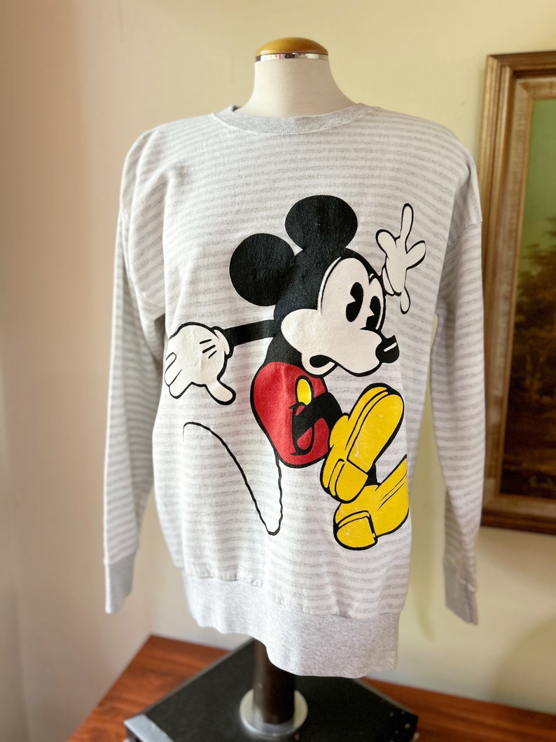 May include: A gray and white striped long-sleeved sweatshirt with a cartoon image of Mickey Mouse in red, black, and yellow.