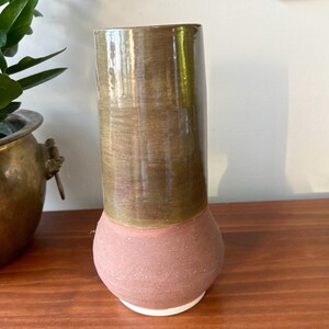 May include: A ceramic vase with a brown and green glaze on the top half and a speckled red glaze on the bottom half. The vase has a white rim.