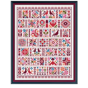 May include: A framed cross-stitch sampler featuring a grid of colorful geometric patterns, floral motifs, and bird figures in shades of red, pink, blue, green, and orange on a white background, enclosed in a dark blue frame with a deep red mat.