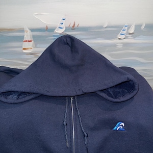 Puede incluir: Una sudadera con capucha azul marino con un pequeño diseño de ola bordado en el pecho izquierdo.