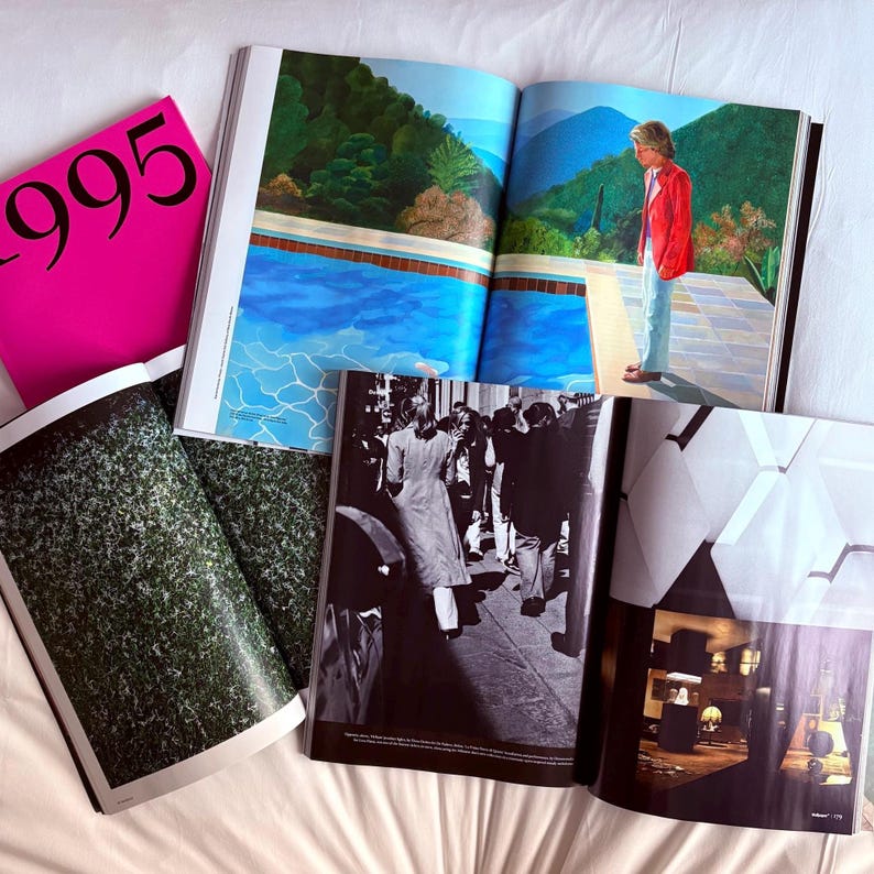 May include: An assortment of open magazines and a pink book with the number "995" printed in black. The magazines display colorful and black and white photographs, including a pool scene and a crowd of people.