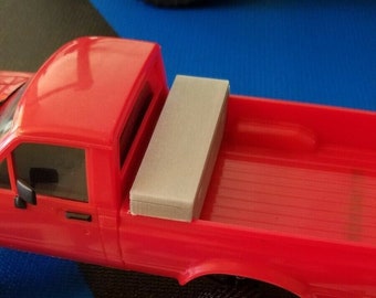 May include: A red toy pickup truck with a gray toolbox in the bed. The truck has black wheels and is sitting on a blue and black mat.