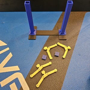 May include: A disassembled, 3D-printed structure with blue vertical supports and yellow, curved components. The base is black, and the components are arranged on a blue and black patterned surface. Small purple squares are also present.