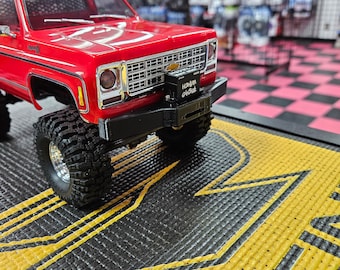 May include: A red toy truck with a black bumper and a black license plate that says "HONDA CIVIC". The truck is sitting on a black and yellow mat.