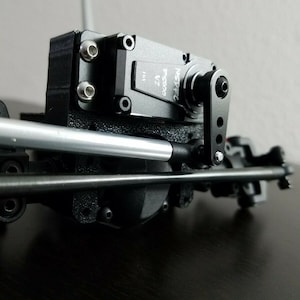 May include: A black and silver servo motor with a black arm attached. The servo motor has the text "INSTAZC PS300 V2" printed on it.