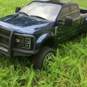 May include: A dark blue pickup truck with a black front bumper and a black grille. The truck is parked in a grassy field.