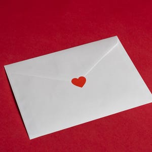 May include: A white envelope with a red heart sticker on a red background. The envelope is sealed and angled, suggesting it contains a message. The image has a romantic or Valentine's Day theme.