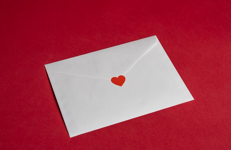 May include: A white envelope with a red heart sticker on a red background. The envelope is sealed and angled, suggesting it contains a message. The image has a romantic or Valentine's Day theme.