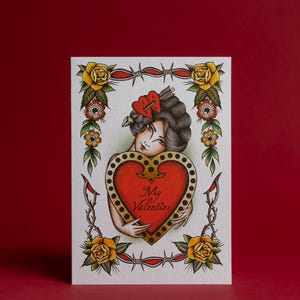 May include: A Valentine's Day card featuring a vintage tattoo-style illustration. The card depicts a woman holding a red heart with the words "My Valentine." The design includes roses, barbed wire, and traditional tattoo elements.