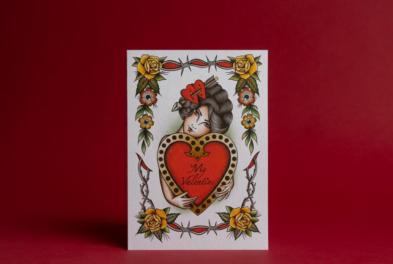May include: A Valentine's Day card featuring a vintage tattoo-style illustration. The card depicts a woman holding a red heart with the words "My Valentine." The design includes roses, barbed wire, and traditional tattoo elements.