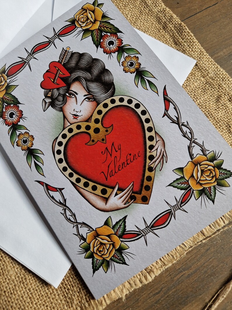 May include: Valentine's Day card featuring a vintage tattoo-style design. The card showcases a woman holding a heart with the words "My Valentine." The design includes roses, barbed wire, and a decorative border, all in a classic tattoo aesthetic.