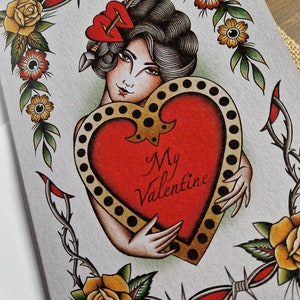 May include: Greeting card featuring a vintage tattoo-style illustration. A woman with dark hair and a red heart-shaped hair accessory embraces a large red heart with the words "My Valentine." The design includes yellow roses, barbed wire, and a decorative border.
