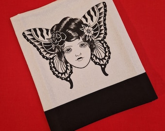 May include: A white tote bag with a black butterfly and a woman's face printed on the front. The bag has a black bottom.