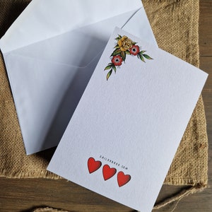 May include: A white stationery set featuring a blank card with a floral corner design and three red hearts. An open white envelope is next to the card. The website address SAILORBROO.COM is printed on the card.