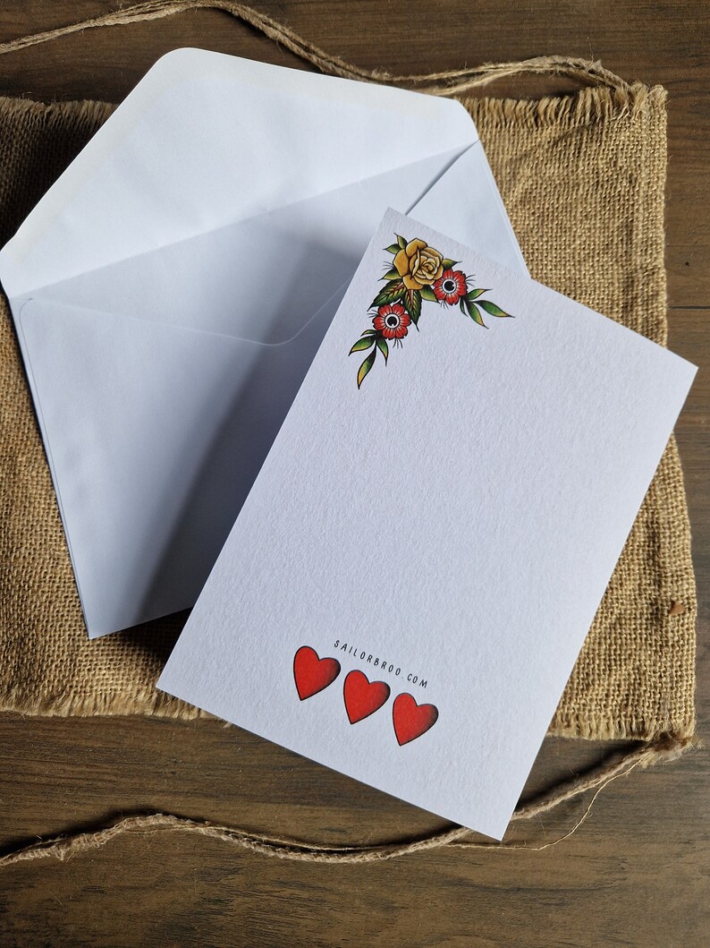 May include: A white stationery set featuring a blank card with a floral corner design and three red hearts. An open white envelope is next to the card. The website address SAILORBROO.COM is printed on the card.